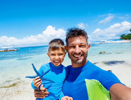 Boy with his father holding a blue starfish on sandy beach, Philippinesの写真素材