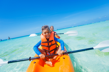 Kids enjoying paddling in orange kayak at tropical ocean water during summer vacationの写真素材