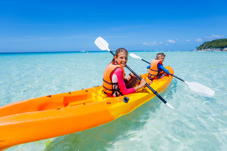 Kids enjoying paddling in orange kayak at tropical ocean water during summer vacationの写真素材