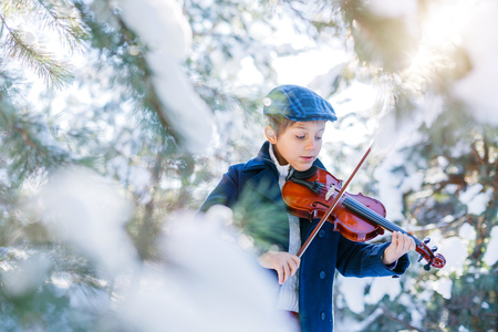 Winter fairy tale. Cute boy violinist in winter forest.の写真素材