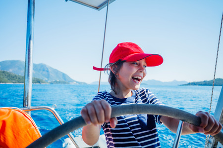 Little boy captain on board of sailing yacht on summer cruise. Travel adventure, yachting with child on family vacation.の写真素材