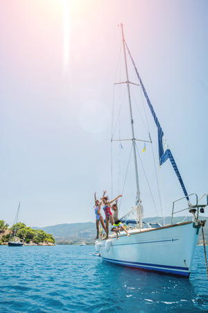 Happy family jump in sea of sailing yacht on summer cruise. Travel adventure, yachting with child on family vacation.の写真素材