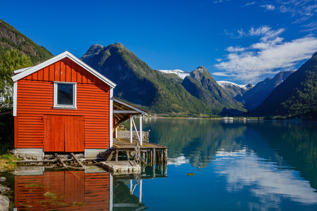 Beautiful red fishing house on fjord. Beautiful nature with blue sky, reflection in water and fishing house. Norwayの写真素材