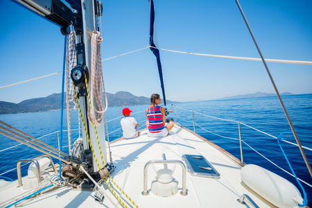 Back view of boy and girl on board of sailing yacht on summer cruise.の写真素材