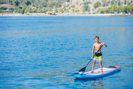 Paddle boarder. Child boy paddling on stand up paddleboard. Healthy lifestyle. Water sport, SUP surfing tourの写真素材