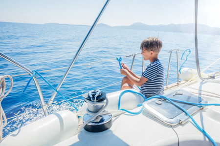 Little boy on board of sailing yacht on summer cruise. Travel adventure, yachting with child on family vacation.の写真素材