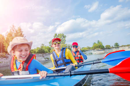 Happy kids kayaking on the river on a sunny day during summer vacationの写真素材