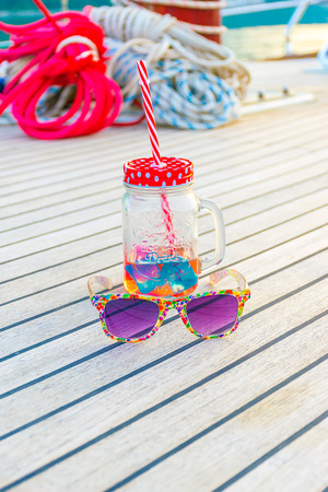 Luxurious purple glasses and an unusual mug with a straw lie on the deck of the yacht during the journey.の写真素材