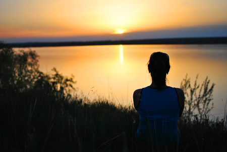 Dreamy girl accompanies a beautiful sunset near the riverの写真素材