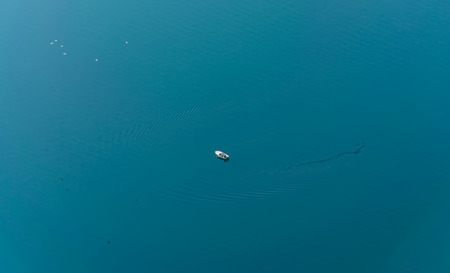 A lone fisherman is fishing from a boat in the middle of the open sea.