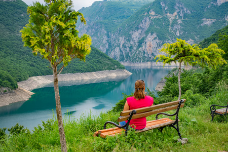 A pretty girl is resting on a bench near the shore of a mountain lake.の写真素材