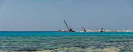 CYPRUS, AYIA THEKLA BEACH - MAY 12/2018: workers are building a breakwater on the shores of the azure sea.の写真素材