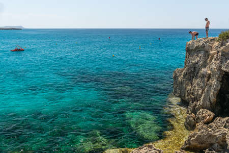 CYPRUS, NISSI BEACH - MAY 12/2018: tourists have fun and jump from a cliff into the azure sea.