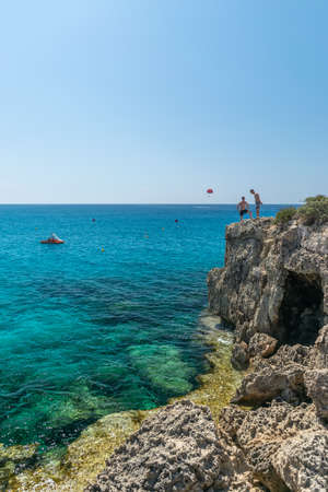 CYPRUS, NISSI BEACH - MAY 12/2018: tourists have fun and jump from a cliff into the azure sea.のeditorial素材