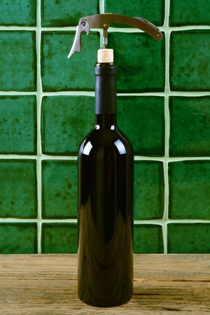Bottle of red wine with corkscrew over green background.の写真素材