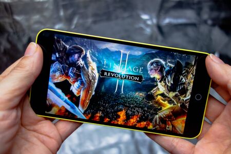 Berdyansk, Ukraine - March 16, 2019: Hands holding a smartphone with lineage 2 revolution game on display screenのeditorial素材