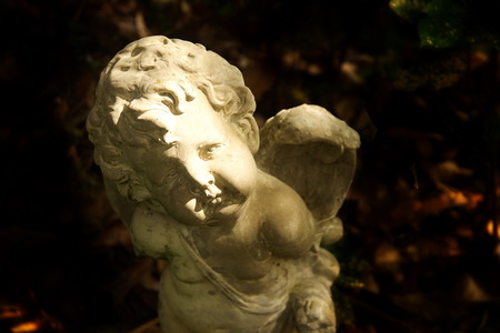 cupid cement sculpture god of love with dark garden backgroundの写真素材
