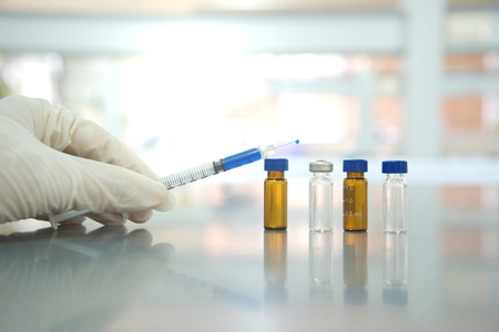 hand with syringe and vial  in science laboratory backgroundの写真素材