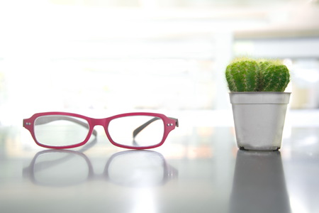 red eye glasses with green cactus in gray pot on office table light backgroundの写真素材