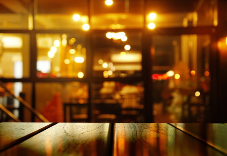 top of reflection wood table with blur orange light party in pub or bar background