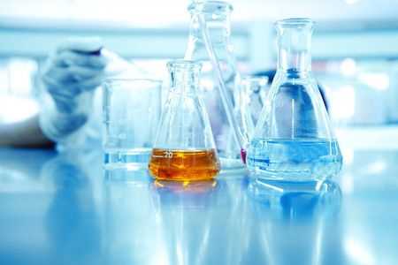 hand of scientist or reseracher drop solution in glass beaker and orange liquid in  flask at blue chemical science laboratory backgroundの写真素材