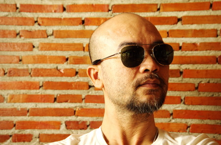 portrait of Asian Japanese cool adult bald beard man wearing sunglasses with brick wall backgroundの写真素材