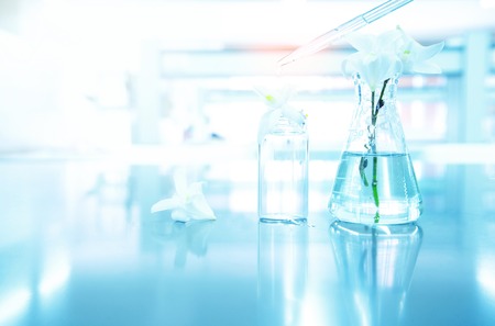 nuture white orchid flower with flask and vial with drop of water in blue biotechnology science backgroundの写真素材