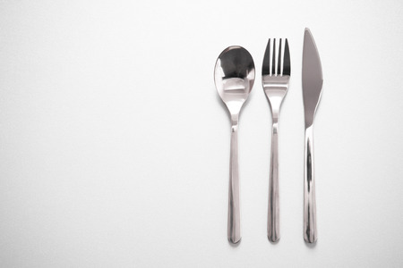 shiny metal silverware of fork knife spoon for eating meal in restaurant grey background