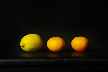 one yellow lemon and two orange fruit for health food in classical vintage still life style with black backgroundの写真素材