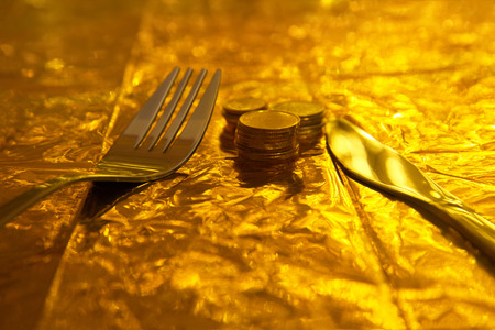 silver fork and knife with coin money on gold dinner background concept of business financial