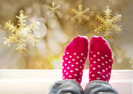 woman feet in cute pink white dot socks at the window with golden snowflake and glowing silver bokeh light Christmas holiday backgroundの写真素材