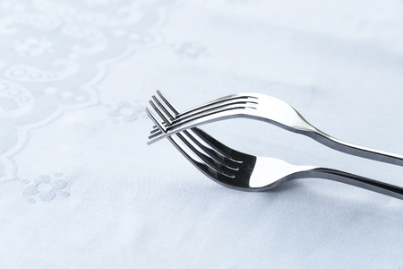 silver metal stainless steel two interaction fork on white tablecloth food luxury dinner background