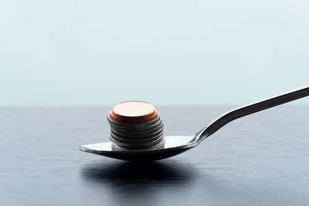 single metal teaspoon with silver and bronze coin money pile for food capitalism business concept financial backgroundの写真素材