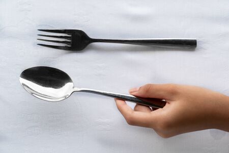 girl hand holding silver spoon and fork on luxury white tablecloth food dining backgroundの写真素材