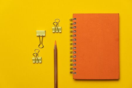 colorful orange notebook with metal yellow clip and wood pencil for office accessory business and education backgroundの写真素材