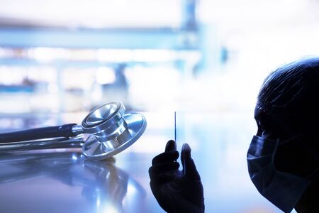 silhouette woman doctor or scientist hand holding test tube with metal stethoscope on table of...