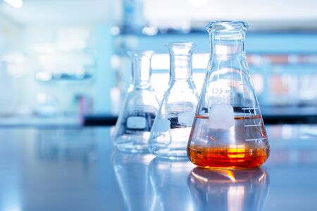 orange solution in science clear glass flask in blue chemistry school laboratory backgroundの写真素材