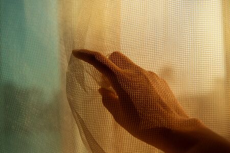 one woman hand under net fabric point finger to the window with orange blue light backgroundの写真素材