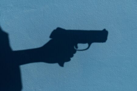 shadow of woman hand holding gun on blue cement wall background in violence crime conceptの写真素材