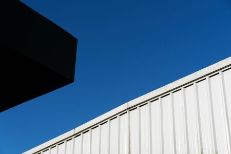 white metal architecture with bright blue sky and part of modern roof black building abstract backgroundの写真素材