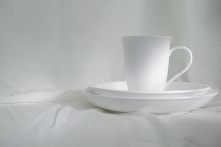 white ceramic cup for hot drink and plate on white fabric classic vintage still life background の写真素材