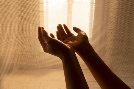 hands of woman pray for religion service with sunlight trough light white curtain background
