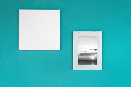 white empty canvas frame with wood frame with black and white seascape picture on bright green blue concrete wall interior backgroundの写真素材