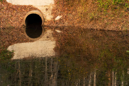 reflection of waste drainage cement pipe in pond water environmental backgroundの写真素材