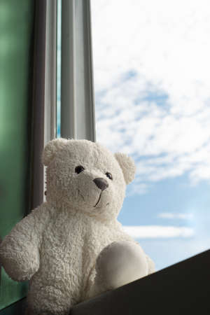 lonely sitting white bear doll on home window with blue skyの写真素材