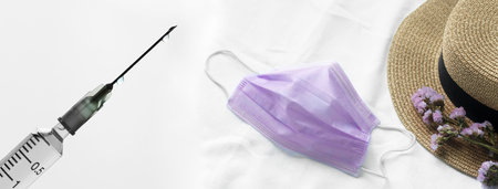 white vaccine syringe and purple face mask with flower woman hat for travel in covid 19 periodの写真素材