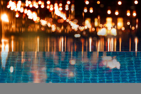 blur red orange light of bar or pub reflection on blue water swimming pool summer party at night backgroundの写真素材