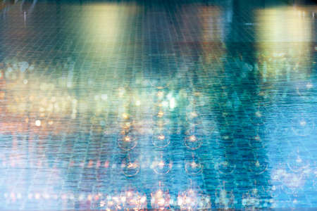 blur glowing  light of bar or pub reflection on blue water swimming pool summer party at night backgroundの写真素材