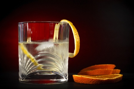 Cold vodka in a glass, with decor oranges and lemon, in black red background, part of art beverage backgroundの写真素材