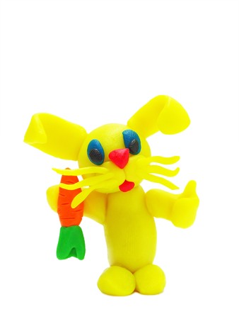 Funny yellow plasticine rabbit with carrot on white background with soft shadowsの写真素材